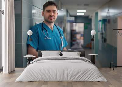 Portrait of confident ER doctor standing in hospital emergency room. Handsome doctor in scrubs holding clipboard, standing in modern private clinic Wall mural