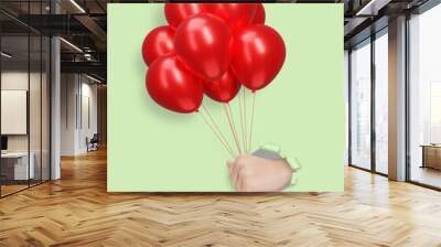 Childrens hand holding red shiny balloons through the hole in mint paper Wall mural