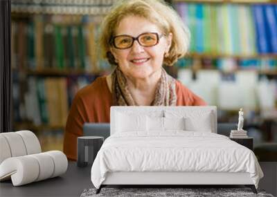 Happy senior woman using laptop in library Wall mural