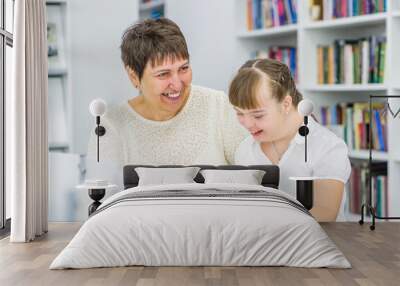 Happy teacher and girl with syndrome down read a book at library. Education for disabled children concept Wall mural