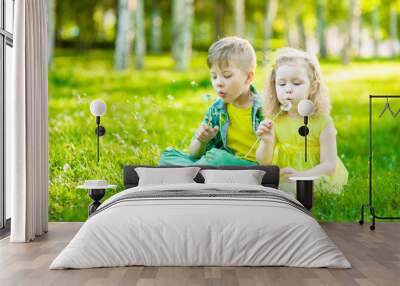 Little girl and boy blowing dandelion together Wall mural