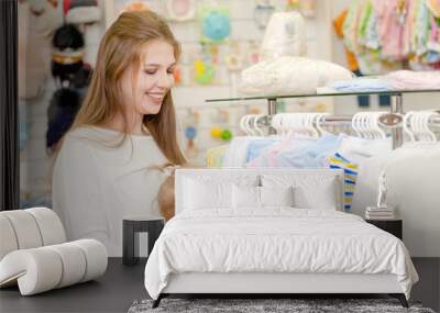 Pregnant woman with a small child choose baby clothes in the store Wall mural