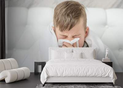 Sick child on bed and blowing his nose in tissue Wall mural