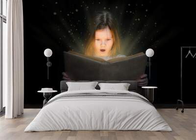 Surprised little girl reading magic book at night on dark background. Empty space for text Wall mural