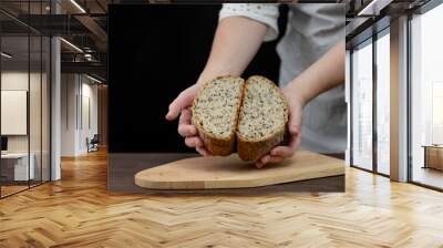 Woman demonstrating a cut  into two halves fresh whole grains warm bread on dark background Wall mural