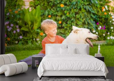 Young boy hugging White Swiss Shepherd dog together on green grass Wall mural