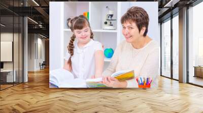 Down syndrome girl with thick dark hair reading a book with her teacher while sitting in a lesson in the classroom Education accessible to children with disabilities concept Wall mural