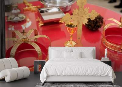 Golden cross, crowns, chalice, and paten on a red church table - wedding or baptism ceremony Wall mural