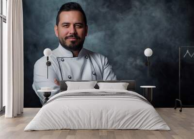 A confident  Hispanic male chef dressed in a white uniform, standing with arms crossed and smiling warmly against a smoky backdrop, showcasing expertise and welcoming nature. Wall mural