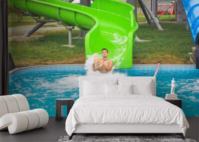 Man go down from water slide to swimming pool in aqua park. Wall mural