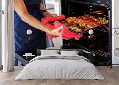 Beautiful young woman preparing meat in oven in the domestic kitchen. Wall mural