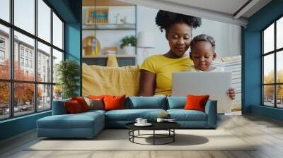 A woman and a child are sitting on a couch, looking at a laptop Wall mural