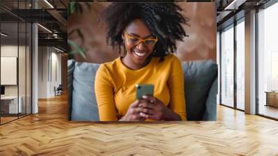 A woman is sitting on a couch and smiling while looking at her cell phone Wall mural