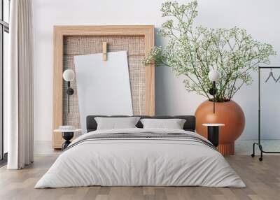 Desk at an empty white wall with a wooden frame with copy space and a vase with white fine flowers Wall mural