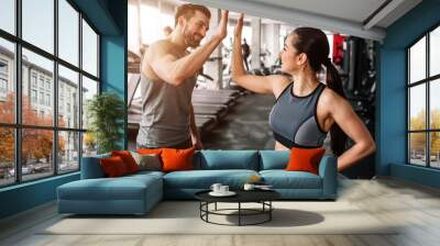 A beautiful girl and her well-built boyfriend are greeting each other with a high-five. They are happy to see each othr in the gym. Young people are ready to start their workout. Wall mural