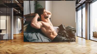 Carefree guy enjoying new day. Sexy, happy bearded man in bed Wall mural