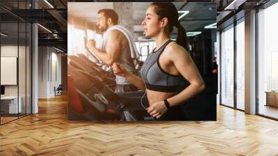 Young man and woman are running on the running machine. They do this exercise every time they come to fitness club.Close up. Cut view. Wall mural