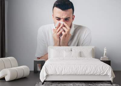 Young man isolated over background. Sick person with nose running. Using white napkin. Coronavirus danger. Ill male person inside studio room. Wall mural