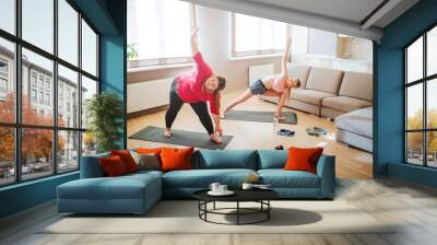 Young plus sixe model and slim woman stretching and exercising together in living room. Standing in yoga pose. One hand up. Dumbbells on floor. Daylight. Wall mural