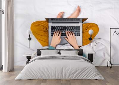 Top view on female hands working on modern laptop from bed at home. Home office or online education concept. Laptop lies on a woman's lap Wall mural