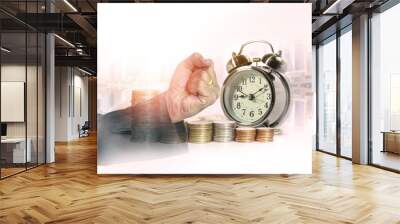 Double exposure of hand of business fist with a row of stack money coins and analog clock on the blurred cityscape background concept for business finances and saving money. Wall mural