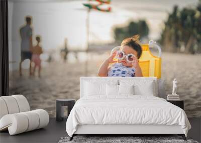 baby in white dress and sunglasses sit on the chair beach yellow color with relaxing and the wind blows in evening time and beautiful sunset light Wall mural