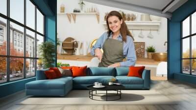 Beautiful young smiling woman preparing vegetable salad at home in modern loft kitchen, slicing a cucumber, copyspace and looking into the camera Wall mural