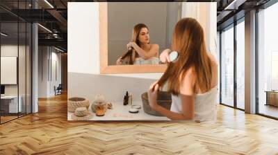 Rear view of a beautiful young woman combing her hair and smiling while looking in the bathroom mirror. Close up Wall mural