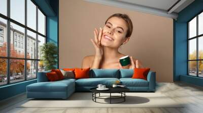 Young woman applies moisturizer to her face and smiles. Skin care concept Wall mural