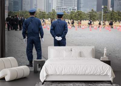 Here in the image two on duty Japanese police officers standing and watching people to maintain law and order in the area. And few people can be seen standing in a queue in the picture. Wall mural