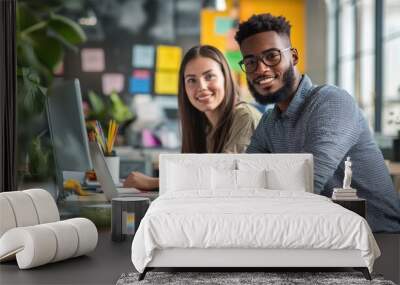 Two coworkers smile as they decorate their workspace with colorful notes and plants, creating a lively atmosphere Wall mural