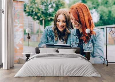 Half length of two young handsome caucasian blonde and redhead straight hair women sitting on a staircase using tablet, looking downward the screen - communication, technology, social network concept Wall mural