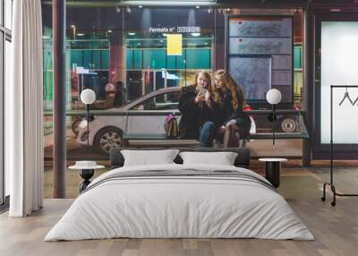 two young beautiful caucasian women friends outdoor in the city night using smart phone hand hold si Wall mural