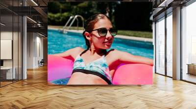 beautiful teenager girl floating on pink donuts in a pool. Wearing sunglasses and smiling. Fun and summer lifestyle Wall mural