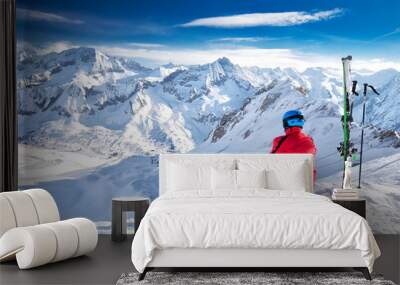 Young happy skier sitting on the top of mountains and enjoying view of Rhaetian Alps, Tonale pass, Italy, Europe. Wall mural