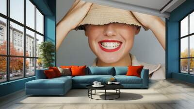 happy girl covering eyes with her hat laughing. Women laughing playfully wearing red lipsitck. Female covering her eyes with a bucket hat laughing. Woman with white teeth laughing. Wall mural