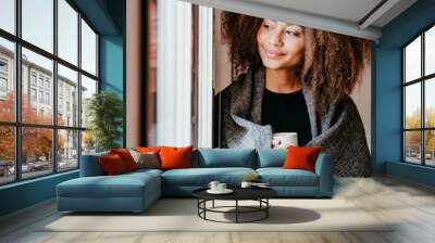 portrait of beautiful afro american young woman by the window holding a cup of coffee. Lifestyle indoors Wall mural