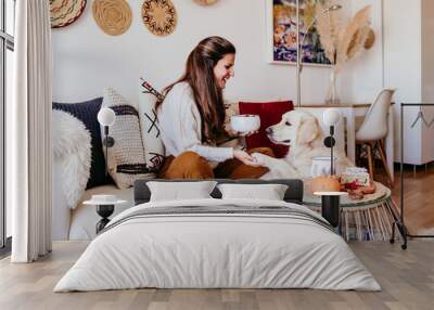 woman having a cup of tea at home during breakfast. Cute golden retriever dog besides. Healthy breakfast with fruits and sweets. lifestyle indoors Wall mural