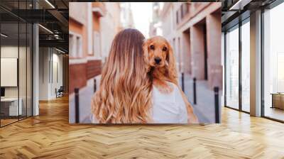 young woman at the street holding with her cute cocker dog on shoulder. Lifestyle outdoors with pets Wall mural