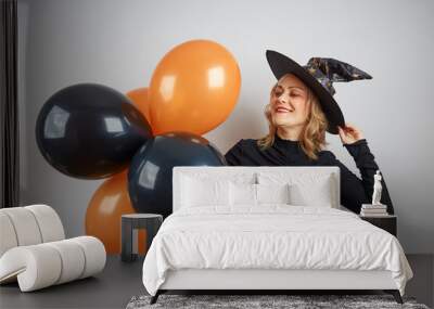 blonde woman in halloween witch costume in a black hat with black-orange balloons on a gray background Wall mural