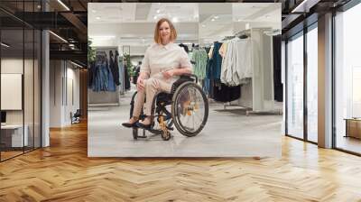 Woman shopper in a wheelchair chooses clothes in the mall. Banner with place for text. Wall mural