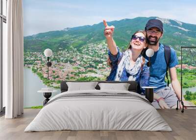 Couple sit in Mtskheta historical site and Caucasian male shows finger up to blank space. Travel holiday background copypaste. Wall mural