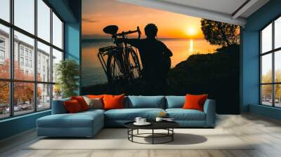 Silhouette of cyclist traveler with his bicycle enjoy sunset view together by tranquil Sevan lake in nature. Bicycle touring outdoors in nature Wall mural