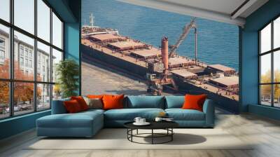 Unloading of a bulk carrier ship in a port on a sunny day Wall mural