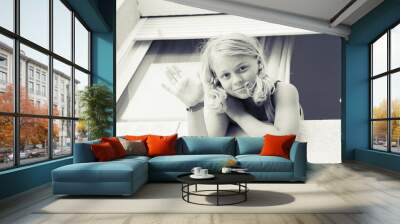 Young blond girl showing hello gesture in the window Wall mural