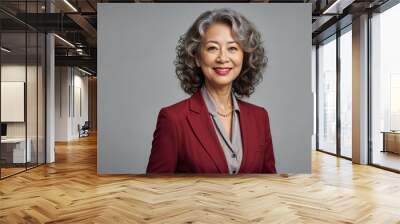 Self-assured and confident mature business woman portrait, she has beautiful curly hair with a hint of grey, red pearl necklace, maroon red blazer, poised in front of a light grey isolated backdrop Wall mural