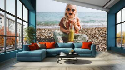 Child drinking smoothie on beach healthy lifestyle summer vacations child with reusable glass bottle vegan organic beverage picnic outdoor kid laughing happy emotions Wall mural