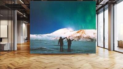 Couple Travelers enjoying Northern lights view above mountains raised hands Travel Lifestyle and relationship man and woman concept vacations into the wild night scene Wall mural