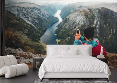 Man traveler using smartphone sitting on mountain summit travel in Norway adventure lifestyle active vacations modern technology connection concept Wall mural