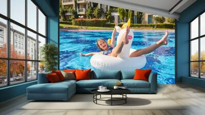 A happy girl in an inflatable circle in the form of a unicorn swims near the hotel. Near the hotel. Swimming pool near the hotel. Summer recreation and entertainment. Blue water. Wall mural